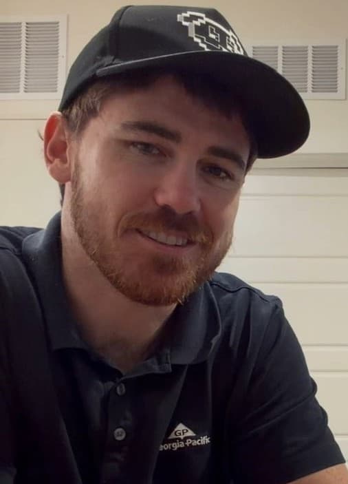 Brice Patterson (Giga) — roots-to-results strategist Brice Patterson (Giga / @gigatronaura) smiling in a black pixel-dog cap and navy polo